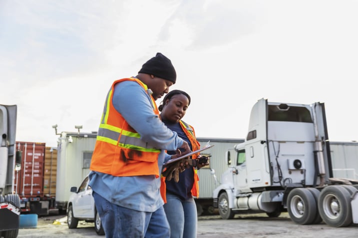 Two truckers talking in a high visibility vests.