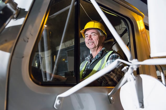 An older truck driver wearing hard hat and visibility vest