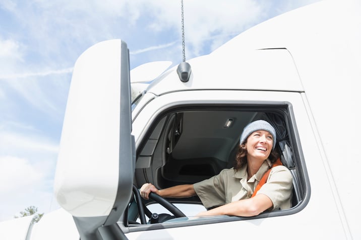 Middle-aged female truck driver looking out driver's window while smiling.