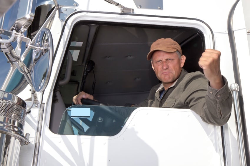 man clenching fist angrily out window of semi truck