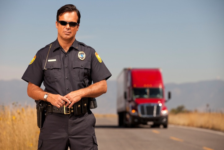a police officer posing standing in front of a semi driving down the road