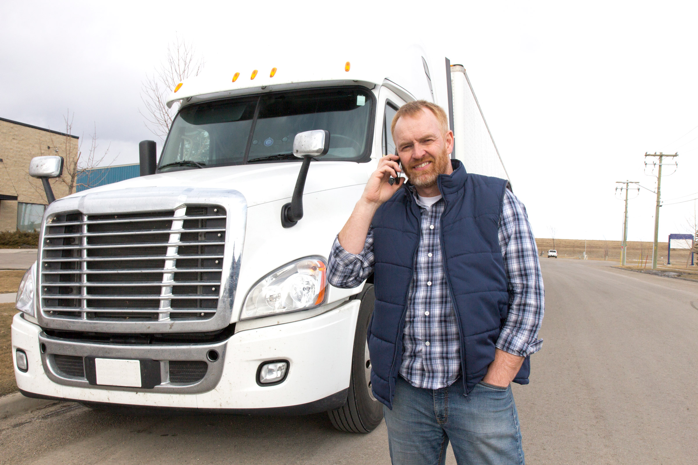a truck driver standing in front of a semi on the phone