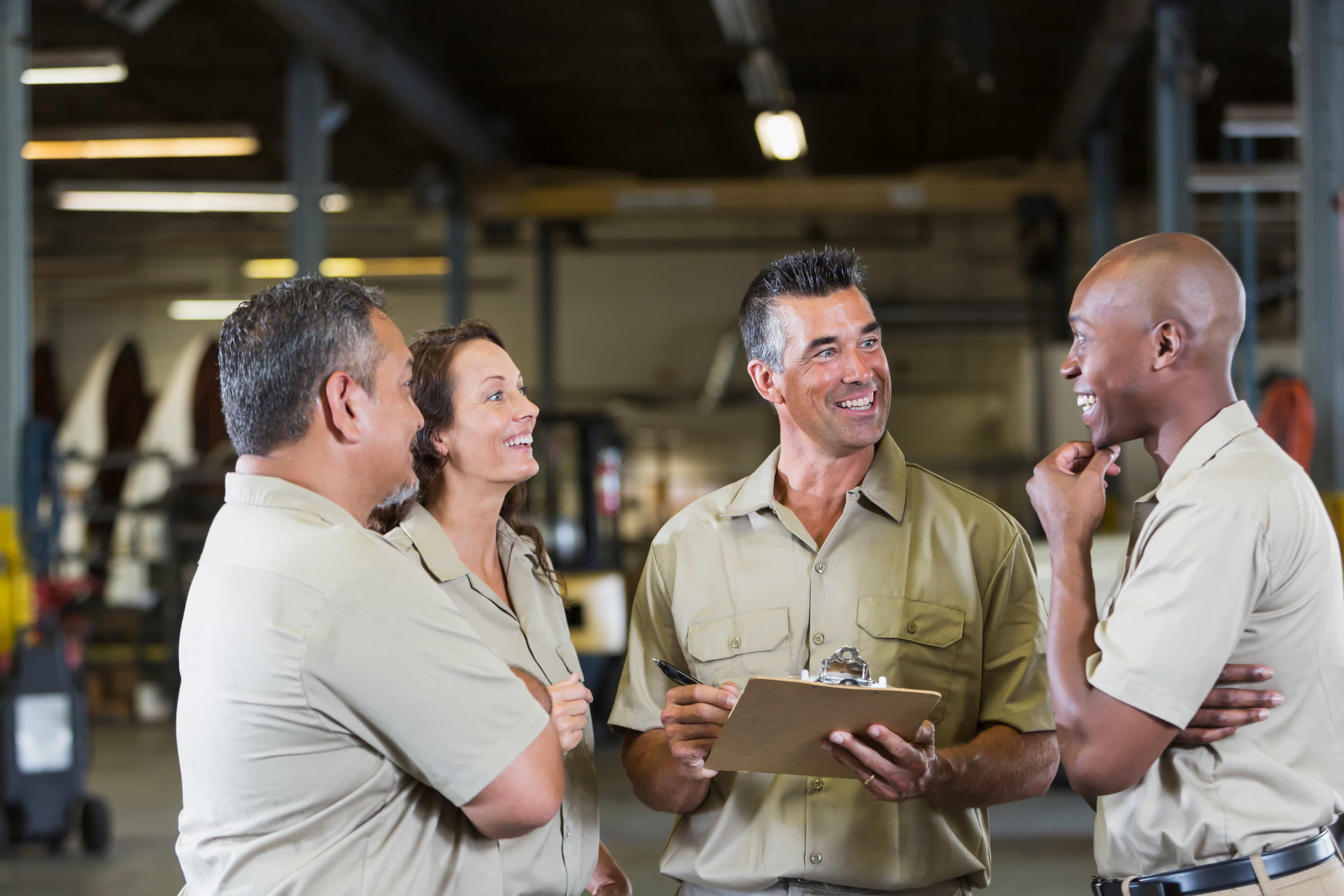 Four workers at a trucking company, standing in a garage, laughing