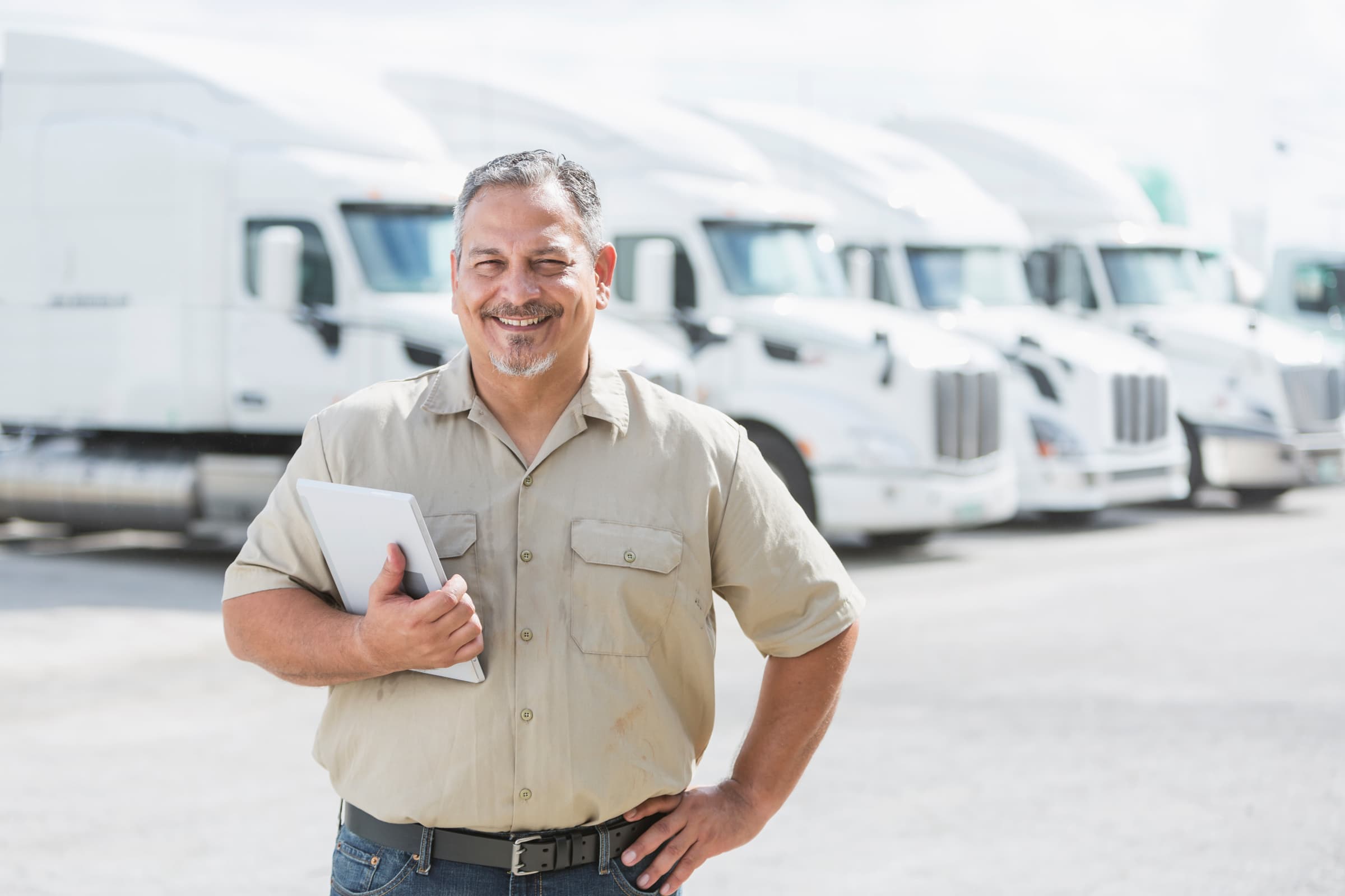 smiling man posing in front of a fleet of trucks holding a tablet 