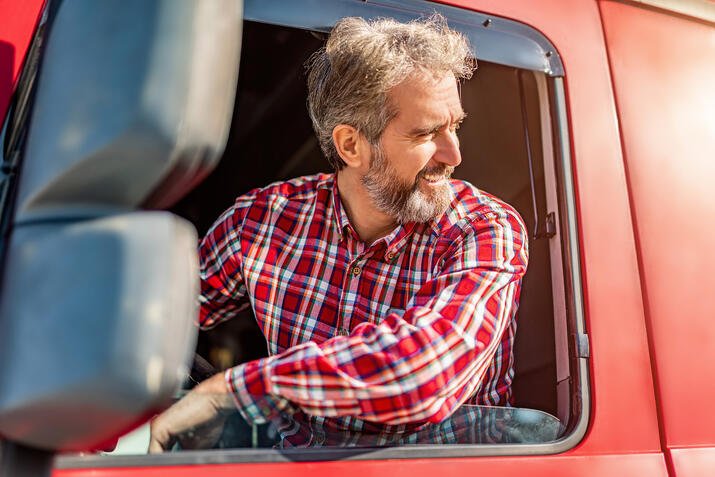 Happy truck driver wearing casual clothing sitting in his truck and parking, looking over shoulder.