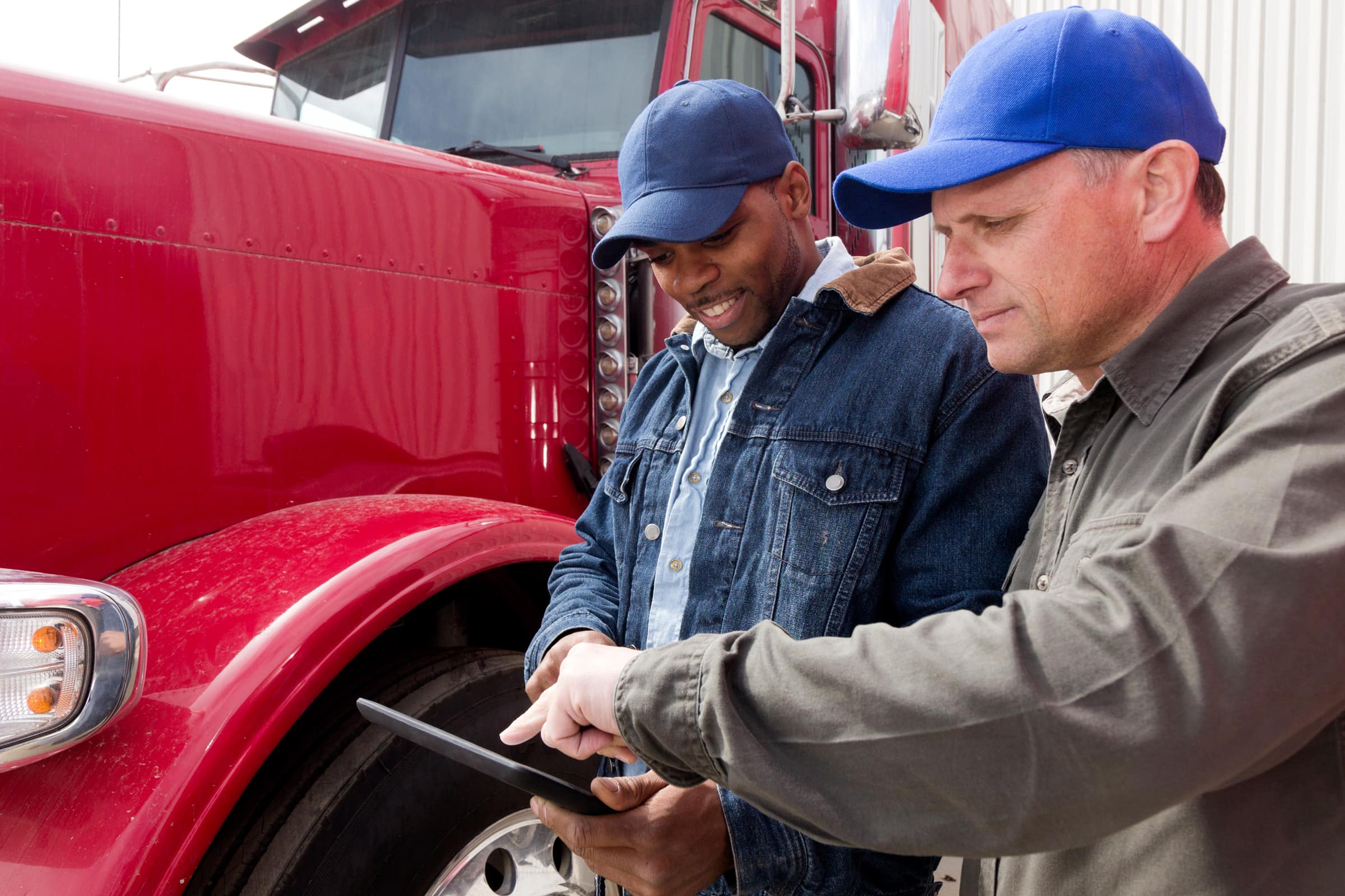 Two truck drivers having a conversation and using a tablet computer in front of a red semi truck 