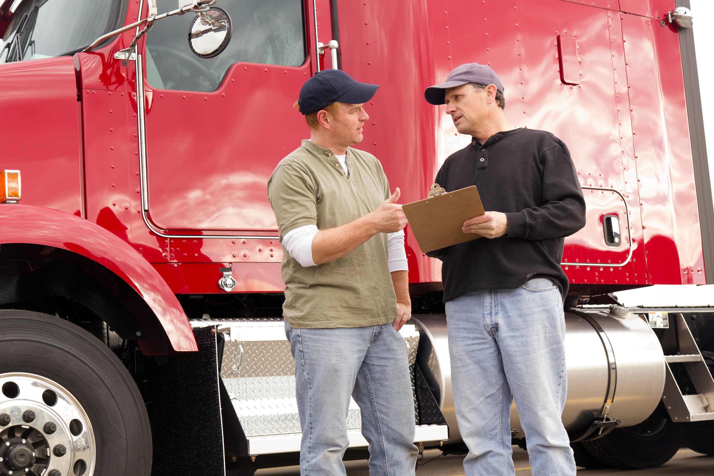 two truck drivers standing by a red semi talking