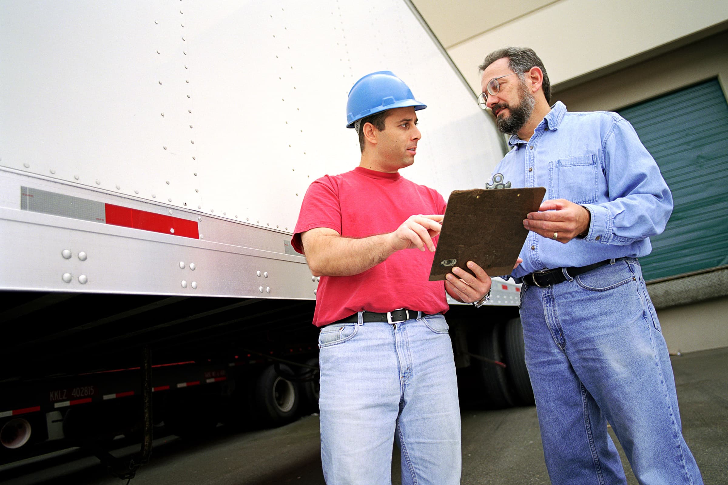 two semi truck drivers talking and holding a clipboard