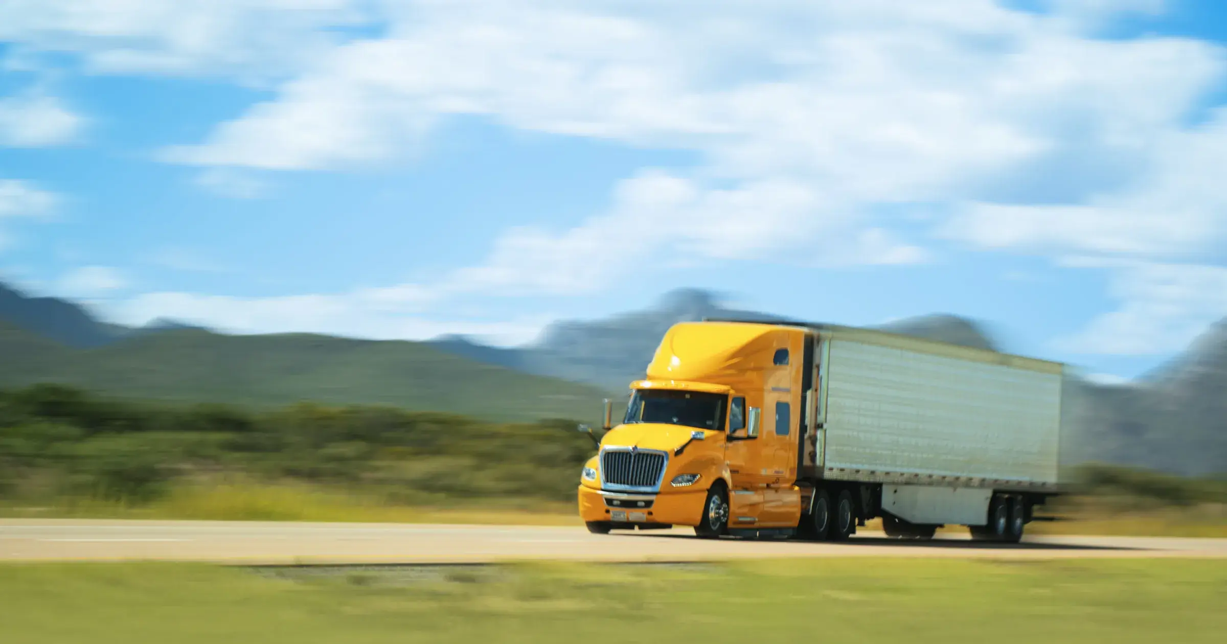 Yellow semi-truck driving through a green road