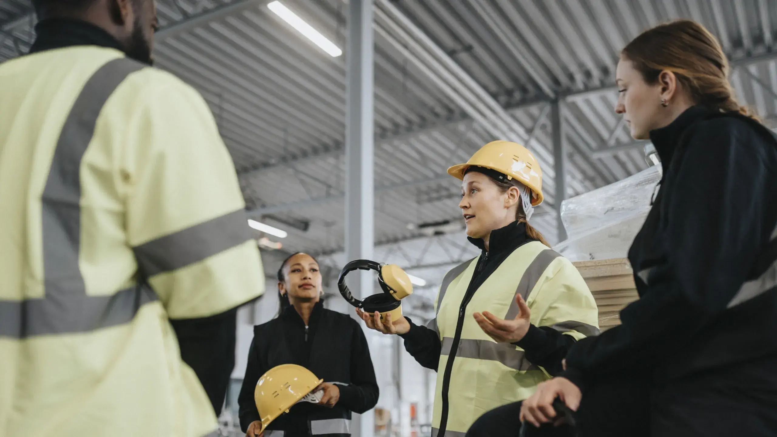 Female worker holding ear protector while discussing with colleagues at distribution warehouse