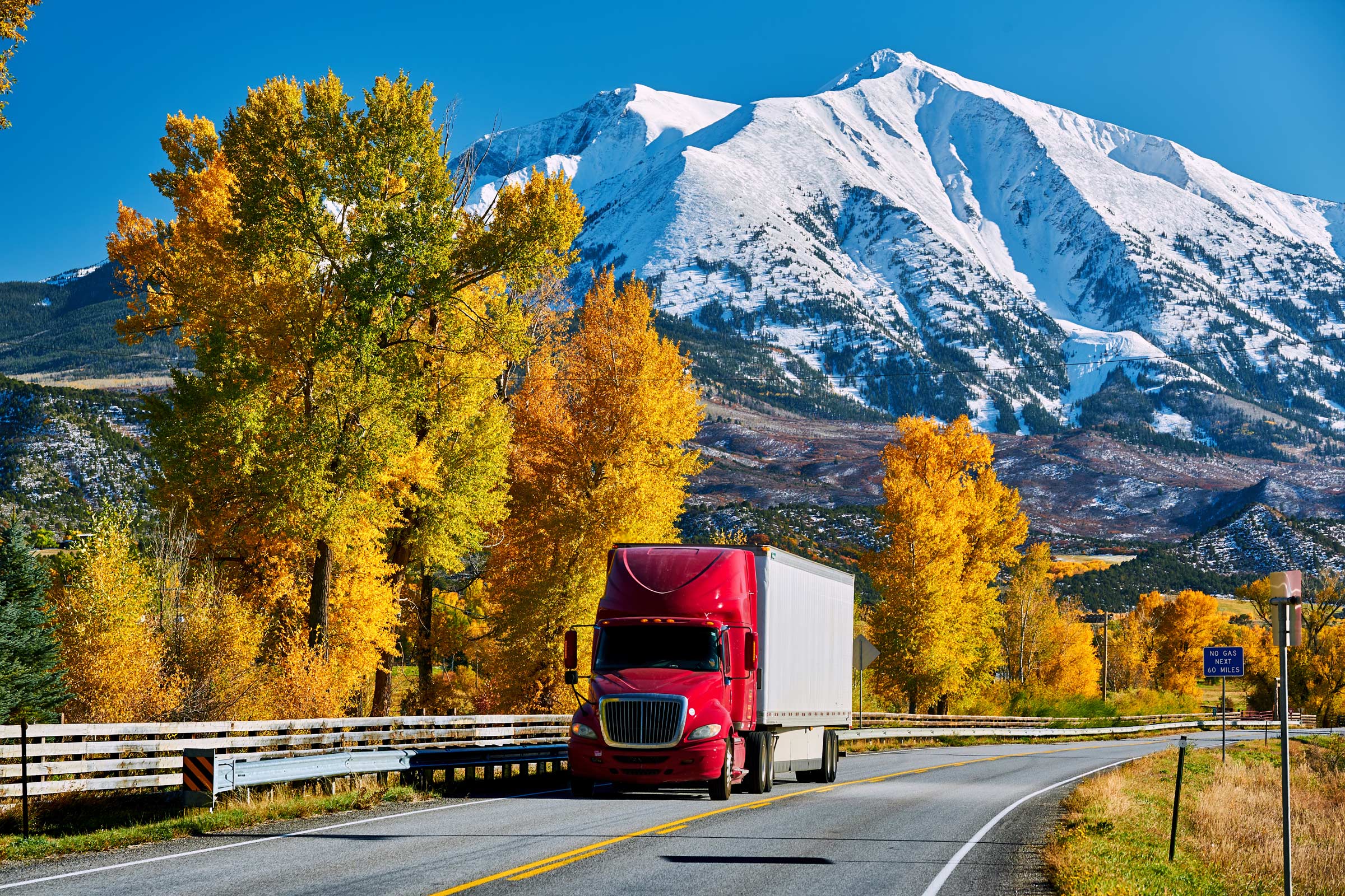 a semi driving on a road through the mountains in fall