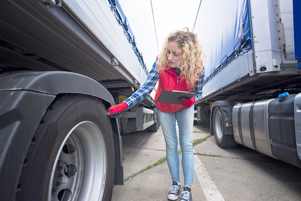 a female safety worker inspecting a tractor trailer tire