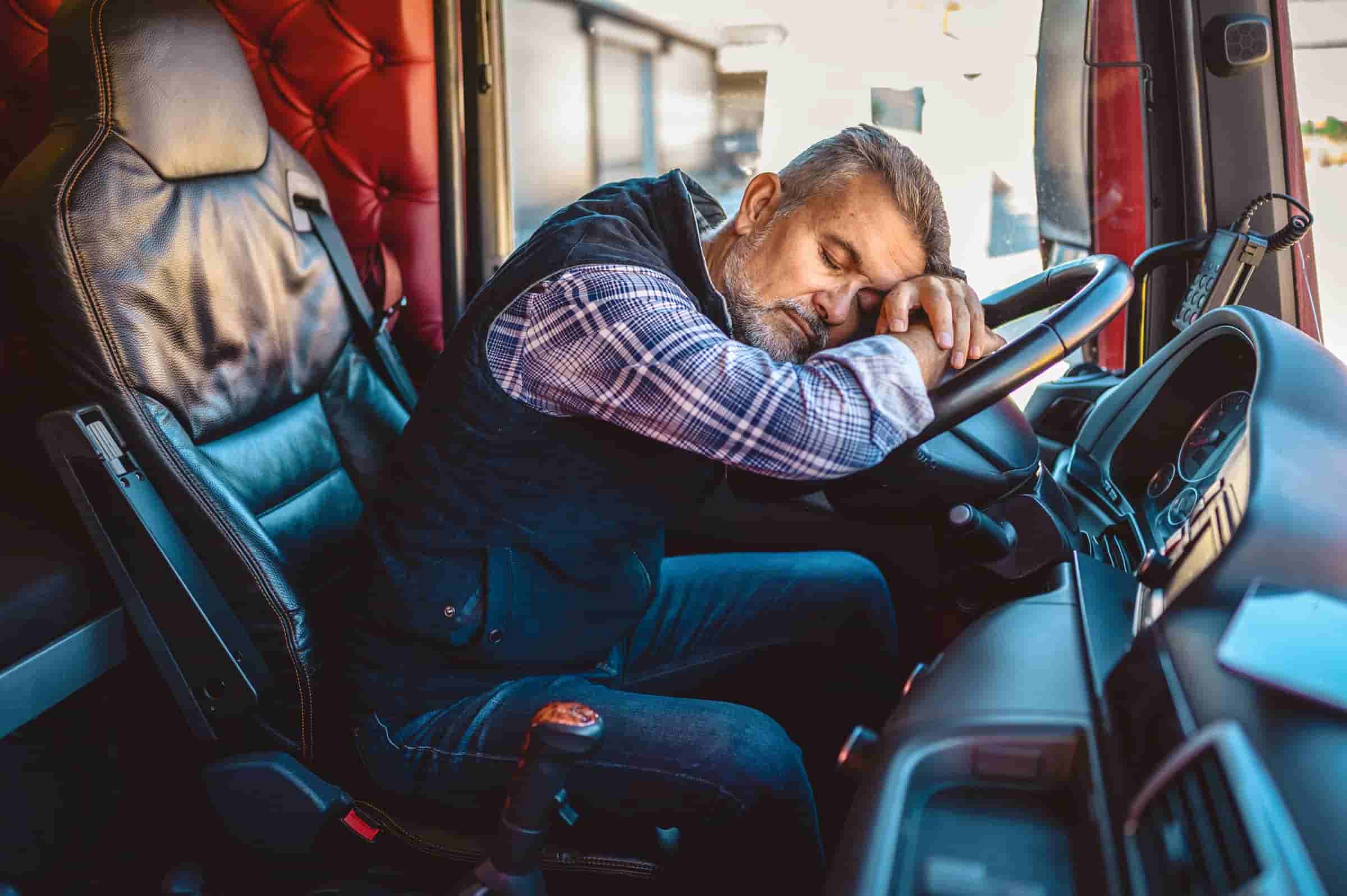 Exhausted truck driver falling asleep on steering wheel.